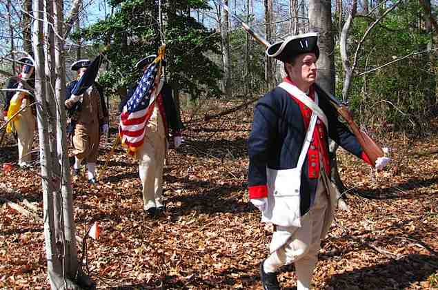 Dan Rolph with his Brown Bess musket leads Guardsmen Andy Johnson, Larry McKinley, and Darrin Schmidt to the gravesite in the woods.