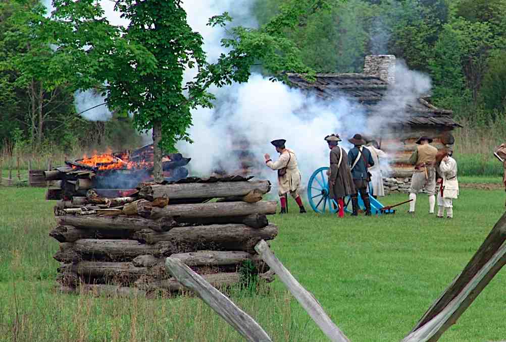 Reenactors fire a cannon as one of the station's structures burns in the background