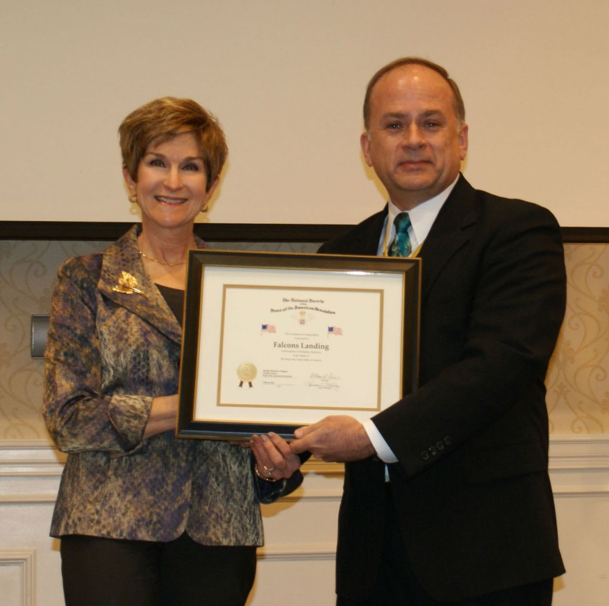 President Bill Price presents a flag certificate to Falcons Landing CEO Barbara Brannon